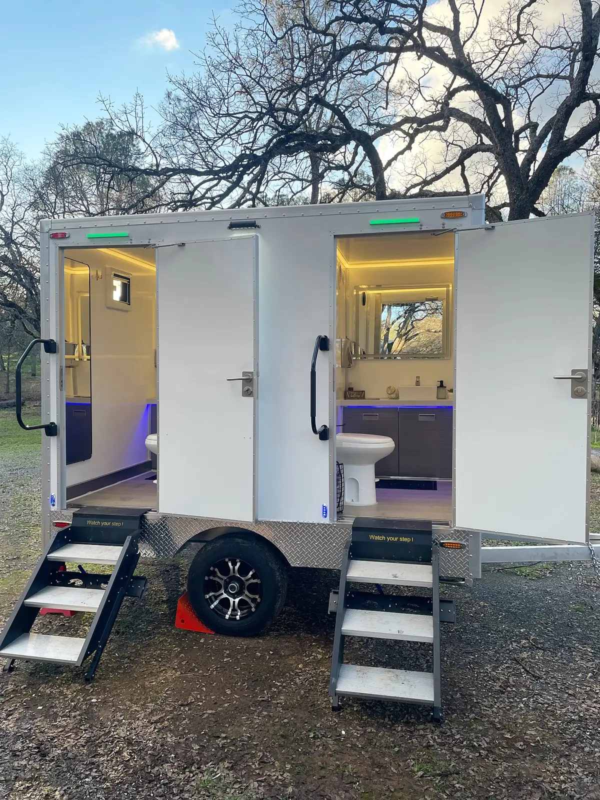 Restroom trailer lit at night with doors open at an outdoor event